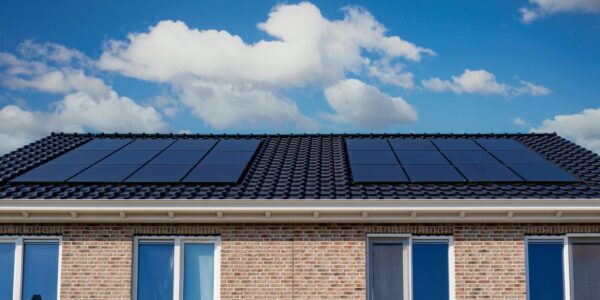 Roof Of A Brick House With Solar Panels Under A Blue Sky With Clouds.