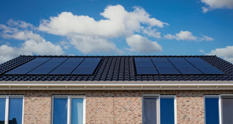 Roof Of A Brick House With Solar Panels Under A Blue Sky With Clouds.